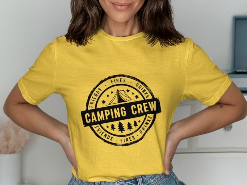 A woman wearing a yellow t-shirt with "Camping Crew" and outdoor-themed graphics, posing indoors.