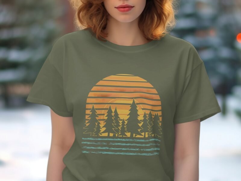 A woman wearing a green t-shirt with a sunset and pine trees graphic, against a blurred outdoor background.