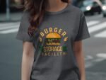 A woman in a gray t-shirt featuring a burger graphic and the words "BURGER STORAGE FACILITY" in colorful text.