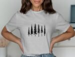 A woman wearing a gray t-shirt with a black forest tree graphic stands with her hands on her hips, smiling.
