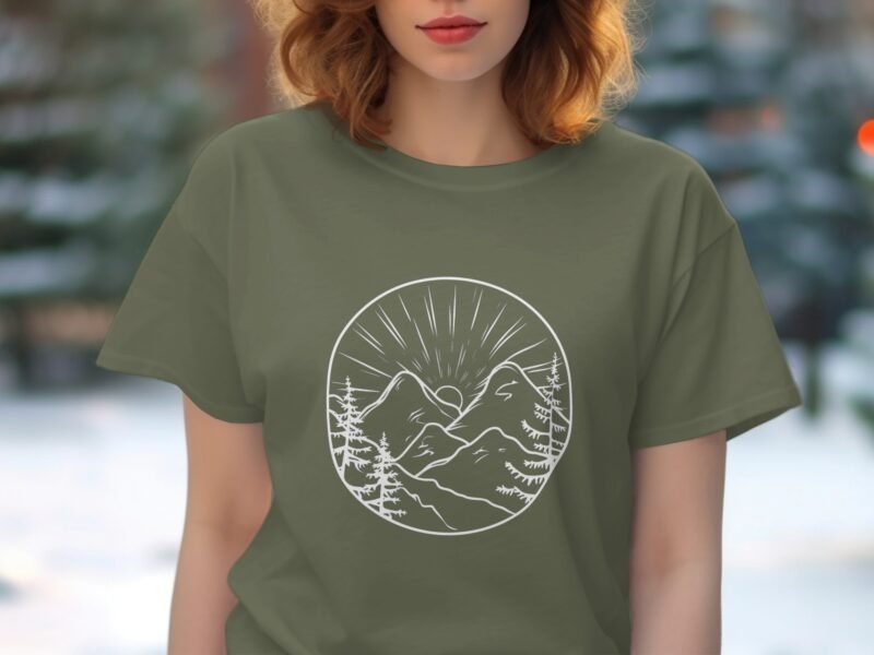 Woman wearing an olive green t-shirt featuring a white mountainous landscape design with trees and sun rays.