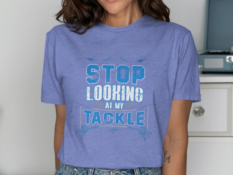 A woman wearing a blue graphic t-shirt that reads "STOP LOOKING AT MY TACKLE" over denim shorts.
