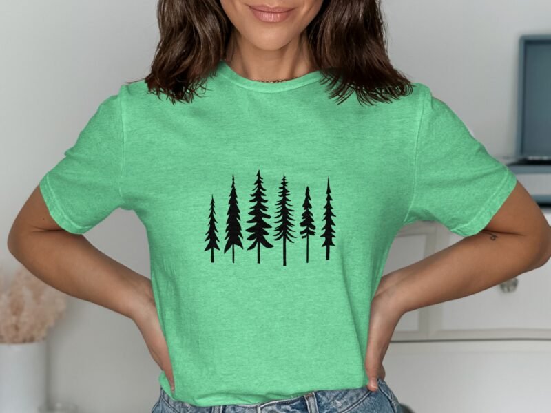A woman poses in a green t-shirt featuring black tree silhouettes, with a neutral background and casual attire.