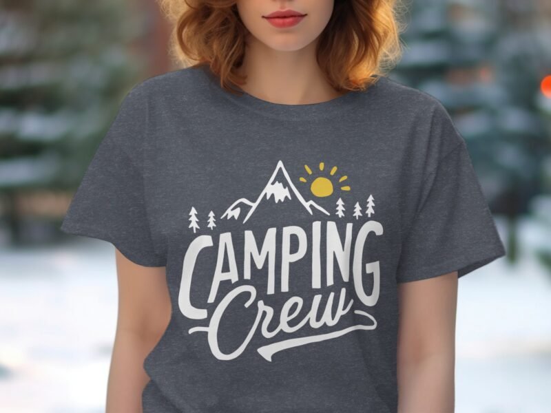 A person wearing a dark gray t-shirt with "Camping Crew" text, mountain, sun, and tree graphics, outdoors.