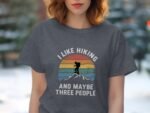 A woman in a gray t-shirt with a hiking graphic and text: "I like hiking AND maybe three people."