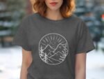 Woman wearing a gray t-shirt featuring a circular mountain and sun design, surrounded by pine trees.