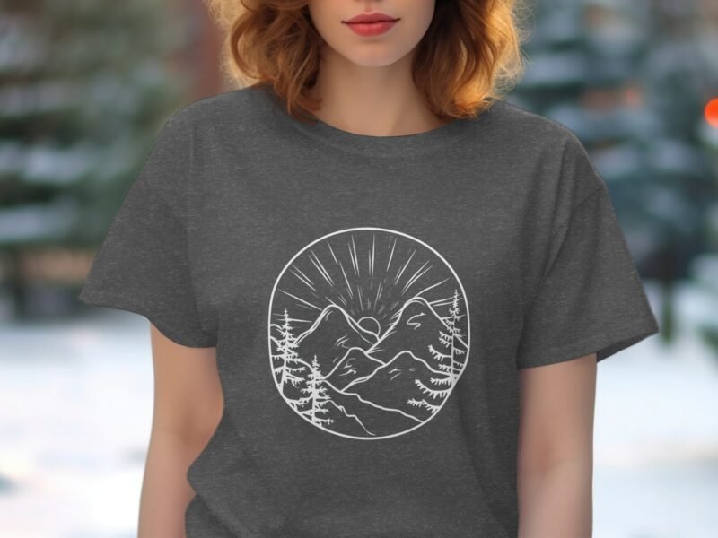Woman wearing a gray t-shirt featuring a circular mountain and sun design, surrounded by pine trees.