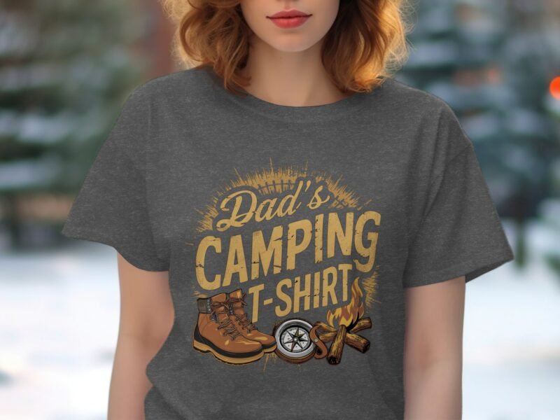 A person with wavy hair wears a gray t-shirt featuring "Dad's Camping T-Shirt" and camping-themed graphics.