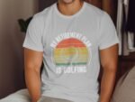 A man in a light gray t-shirt with the text "MY RETIREMENT PLAN IS GOLFING" and a graphic of a golf ball and sun.