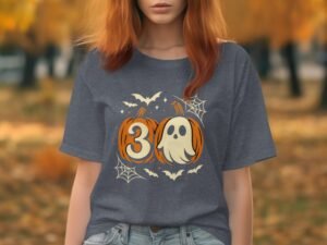Woman wearing a gray Halloween-themed shirt featuring pumpkins, a ghost, and bats, set against an autumn background.