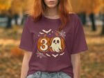 A young woman in a maroon t-shirt featuring a pumpkin and ghost graphic, set against an autumn landscape.