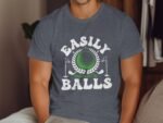 A man in a gray shirt with the text "EASILY Distracted By BALLS" featuring a golf theme and graphic elements.