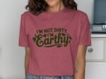 Woman wearing a pink t-shirt with green text that reads "I'm Not Dirty, I'm Earthy." Background includes furniture.