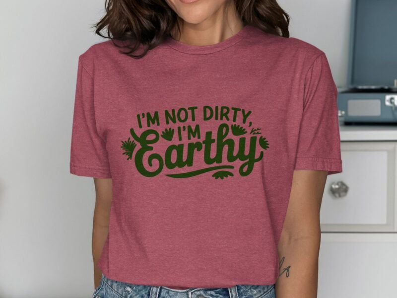 Woman wearing a pink t-shirt with green text that reads "I'm Not Dirty, I'm Earthy." Background includes furniture.