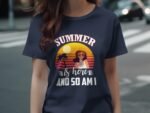 A woman wearing a navy t-shirt with a graphic featuring the text "SUMMER is here AND SO AM I" and a sunset illustration.