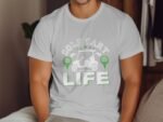 A man in a white t-shirt featuring a "Golf Cart Life" graphic with golf-related imagery and green accents.