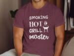 A man sits wearing a maroon t-shirt with the text "SMOKING HOT GRILL MASTER" and a graphic of a grill.