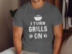 Man wearing a gray T-shirt with the text "I TURN GRILLS ON" and a graphic of a grill, sitting on a couch.