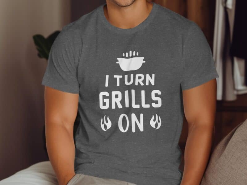 Man wearing a gray T-shirt with the text "I TURN GRILLS ON" and a graphic of a grill, sitting on a couch.