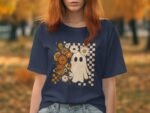 A woman with red hair wears a navy t-shirt featuring a ghost design surrounded by flowers, set against an autumn backdrop.