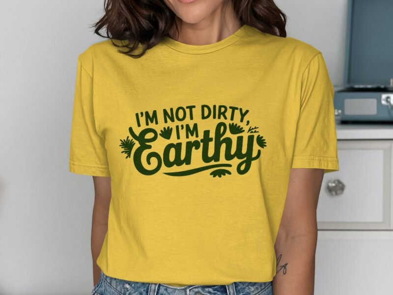 A woman wears a yellow t-shirt with the text "I'm not dirty, I'm Earthy" in green, smiling in a well-lit room.