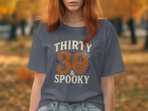 Woman with red hair wearing a gray t-shirt that reads "Thirty & Spooky" with a pumpkin graphic, autumn background.