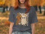 A person with reddish hair wears a gray t-shirt featuring a ghost graphic and floral design against an autumn background.