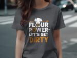A woman wearing a gray t-shirt with "Flour Power - Let's Get Dirty" printed in bold, playful letters.