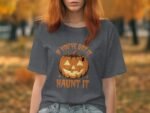 Woman in a gray t-shirt featuring a smiling jack-o'-lantern design with the text "If you've got it, haunt it."