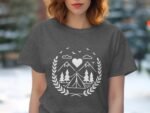 A woman in a gray t-shirt with a white camping-themed graphic, featuring mountains, trees, and a heart.
