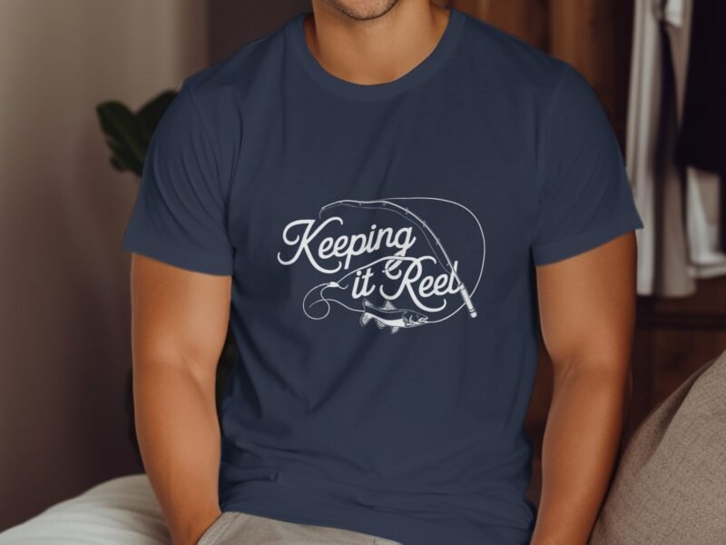 A man in a navy shirt with the phrase "Keeping it Reel" and a fishing rod graphic, sitting against a wooden backdrop.