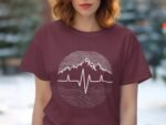 A woman wearing a maroon t-shirt with a mountain and heartbeat graphic, standing outdoors with a blurred background.