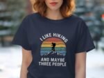 A woman wears a navy t-shirt featuring a hiking graphic and the text, "I like hiking and maybe three people."