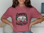 A person wearing a maroon t-shirt with a camping-themed graphic featuring a trailer, trees, and the text "Camping is my Happy Place."