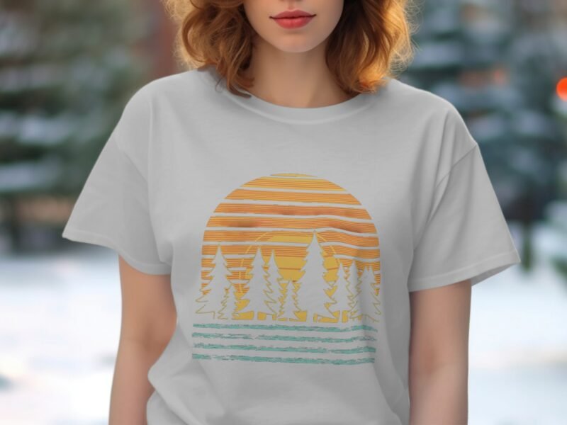 A woman with shoulder-length hair wearing a light gray t-shirt featuring a sunset and tree design.