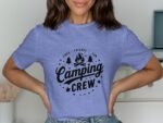 A woman wearing a light purple t-shirt with a "Camping Crew" graphic, surrounded by trees and a campfire design.