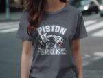 A woman is wearing a dark gray t-shirt with "PISTON BROKE" printed in bold letters and two bottles illustrated below.