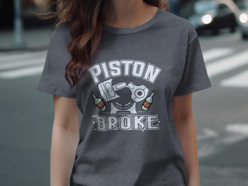 A woman is wearing a dark gray t-shirt with "PISTON BROKE" printed in bold letters and two bottles illustrated below.