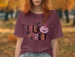 A woman with red hair wears a maroon shirt featuring “TRICK or TREAT” design with bats and a pumpkin in a park.