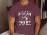 A person wearing a burgundy t-shirt with "Lucky Fishing Shirt Do Not Wash" and a fish graphic, sitting indoors.