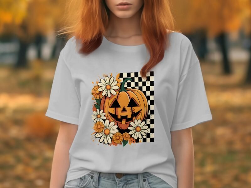 A woman in a white t-shirt with a pumpkin and flower design stands outdoors among autumn foliage.