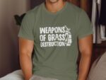 Man sitting on a couch wearing an olive green t-shirt with "WEAPONS OF GRASS DESTRUCTION" and a golf bag graphic.