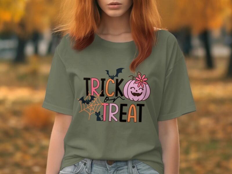 A person wearing a green shirt with "TRICK or TREAT" text, featuring bats and a smiling pumpkin design, in an autumn setting.
