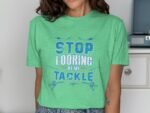 Woman wearing a green t-shirt with the text "STOP LOOKING AT MY TACKLE" in bold blue lettering.