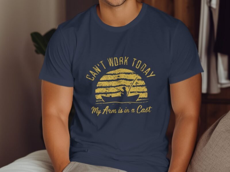 A man in a navy t-shirt with the text "Can’t Work Today, My Arm is in a Cast" and a graphic of a sailboat at sunset.