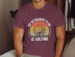 A man in a maroon t-shirt featuring the text "MY RETIREMENT PLAN IS GOLFING" with a graphic of a golf ball and sunset.