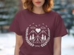 Woman wearing a maroon t-shirt featuring a white camping-themed graphic with mountains, trees, and a heart.