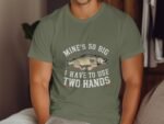 Man wearing an olive green t-shirt with a humorous fish graphic and text: "MINE'S SO BIG I HAVE TO USE TWO HANDS."