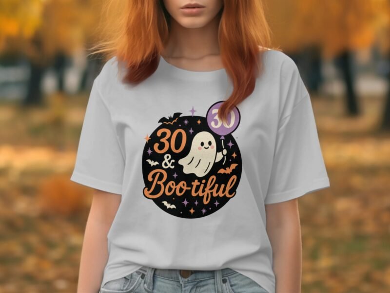 A woman wears a light gray t-shirt with a Halloween-themed design reading "30 & Bootiful," featuring a ghost and bats.