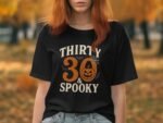 A person with red hair wears a black t-shirt that says "THIRTY 30 & SPOOKY" with Halloween-themed graphics.